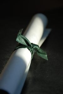 Close up of a rolled-up diploma tied with a green ribbon.