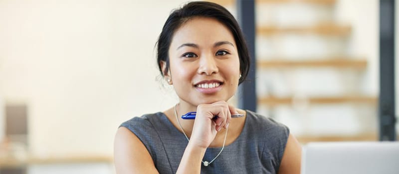A young Asian woman is sitting in front of a laptop computer smiling, possibly because she's satisfied with her progress in the online courses she's taking in Alberta through the Centre for Distance Education